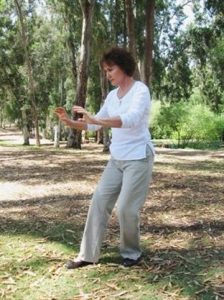 פנינה מתוק בתנוחת צ'י קונג בין עצים גבוהים בשמש