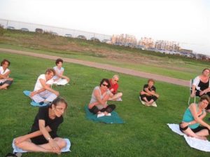קבוצה יושבת על הדשא ומבצעת סיבוב גוף עם ידיים מוצלבות