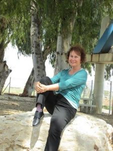 פנינה מתוק יושבת על סלע גדול תחת עצי איקליפטוס